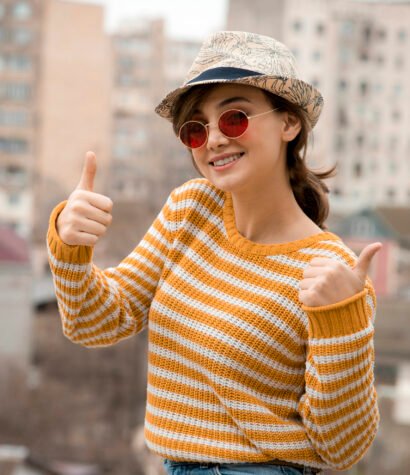 A young cute woman in a cap and glasses posing in outside and showing thumbs up . High quality photo