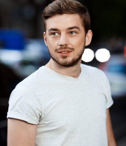 Close up portrait of confident handsome young man in white t-shirt looking away on blurry outdoor background